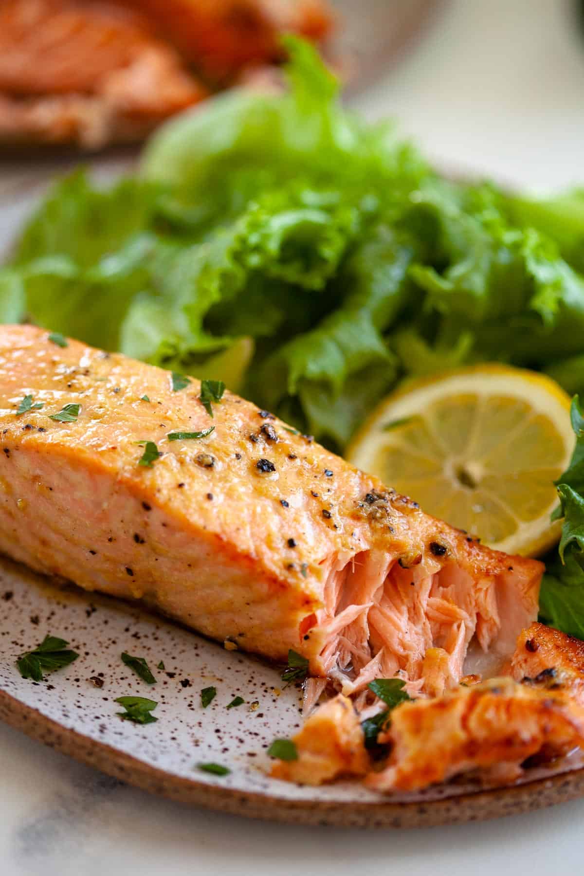 piece of air fryer salmon with herbs and pepper on plate with bed of lettuce and lemon