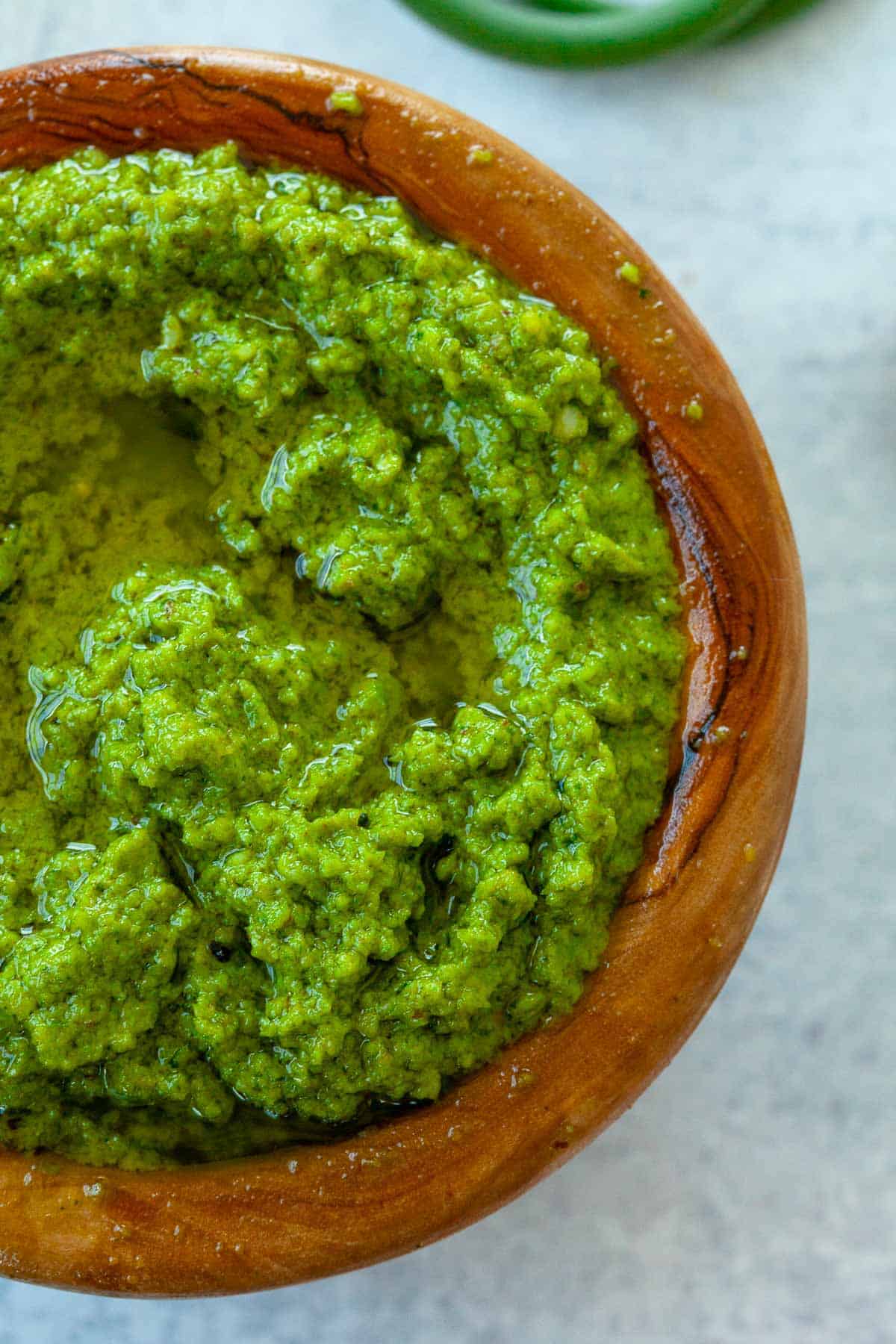 garlic scape pesto with olive oil in small brown wood bowl