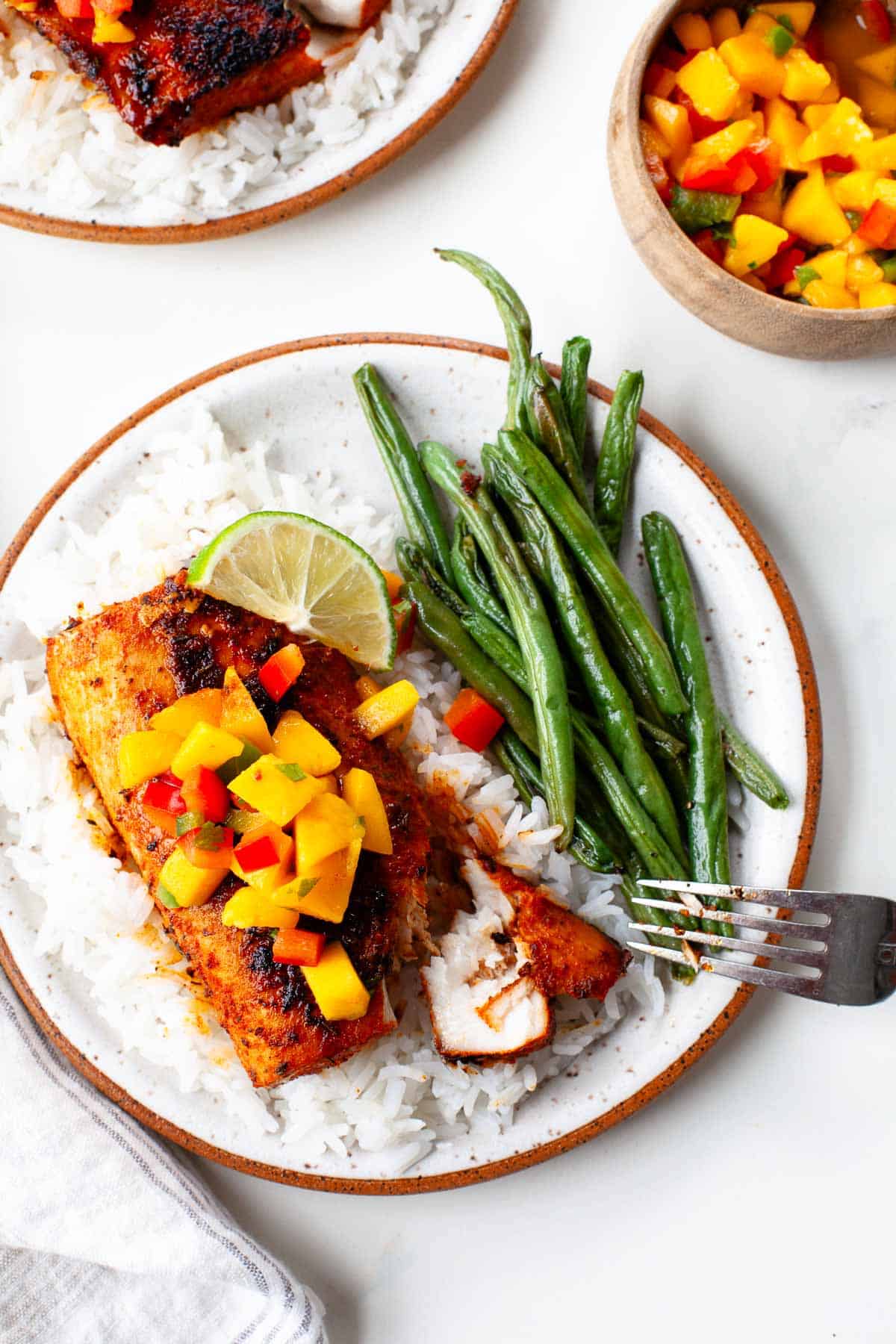 blackened mahi mahi served on a specked plate with white rice, green beans, and fresh mango salsa